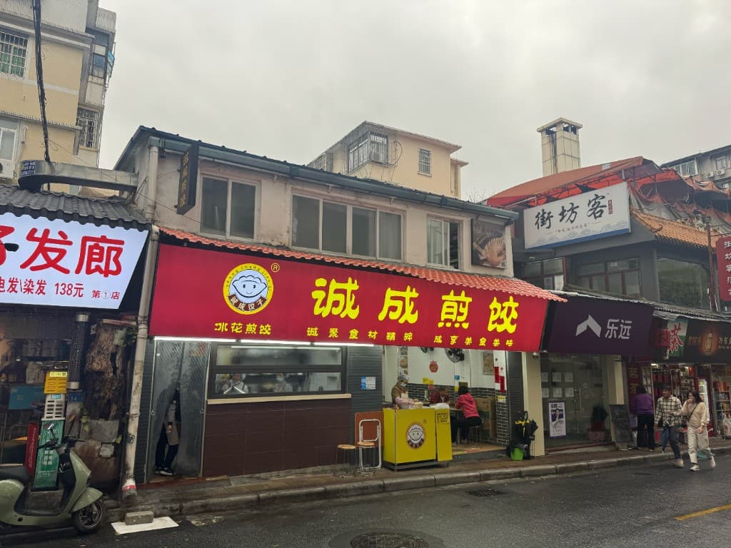 2025 年万松园诚成煎饺门店，红色招牌与冰花煎饺字样，街边照常营业
