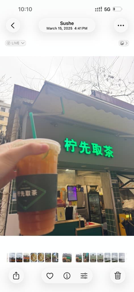 2025 年柠先取茶门店前，手持一杯柠茶，绿色霓虹招牌与杯套上的「柠先取茶」字样